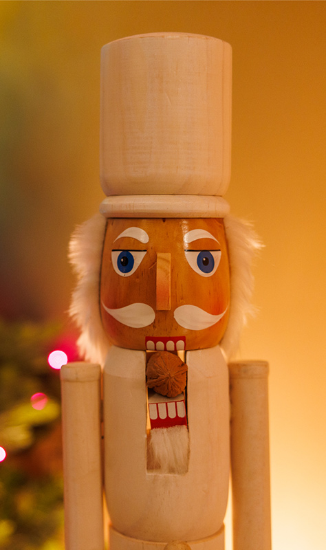 Nutcracker in white in front of holiday decorations.