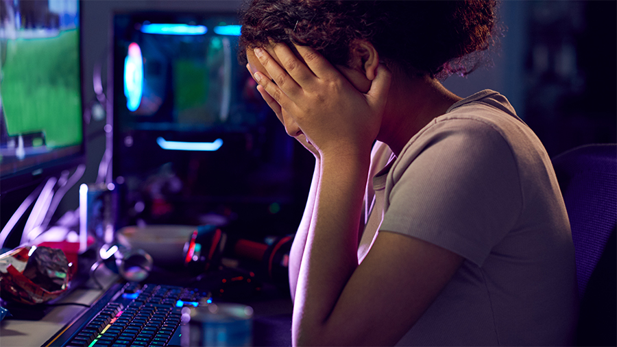 Youth with hands on her head in front of computer, reacting to cyberbullying