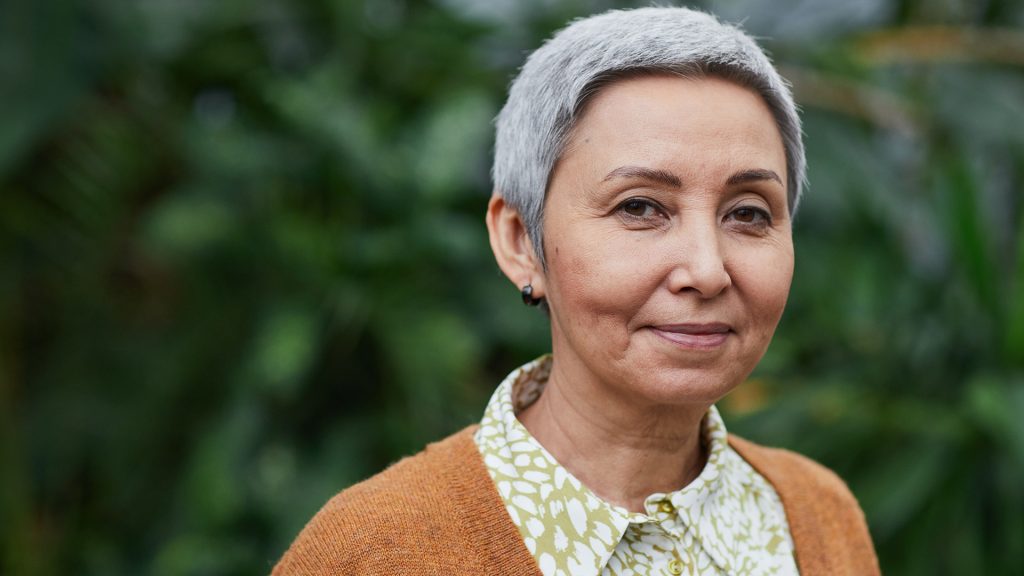 Older person with short grey hair is standing outside and looking directly into the camera.