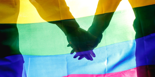 Holding hands behind rainbow flag