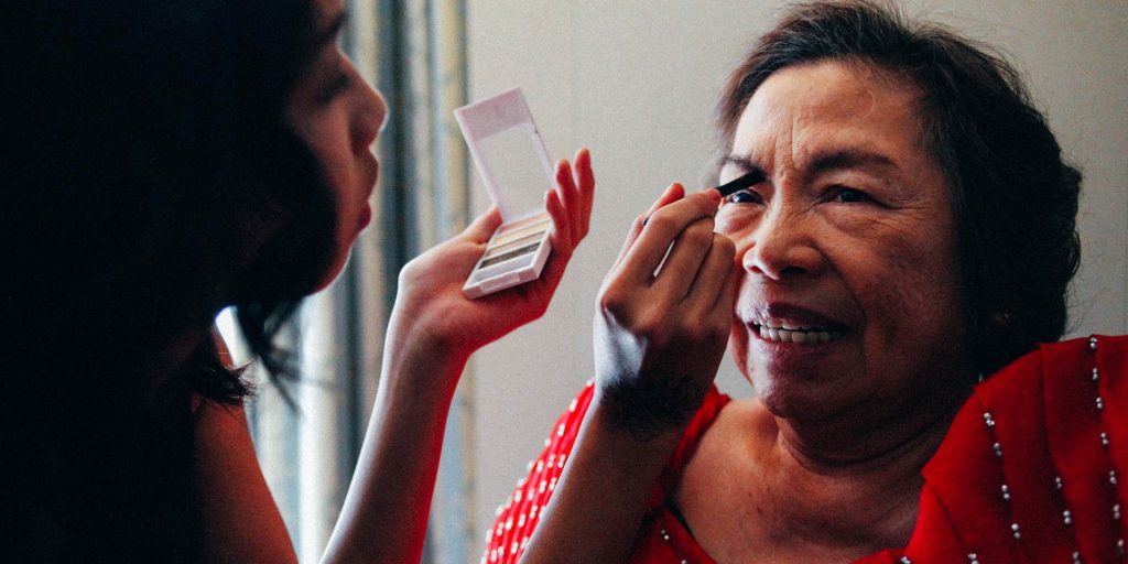 Older adult women having makeup applied by younger carer