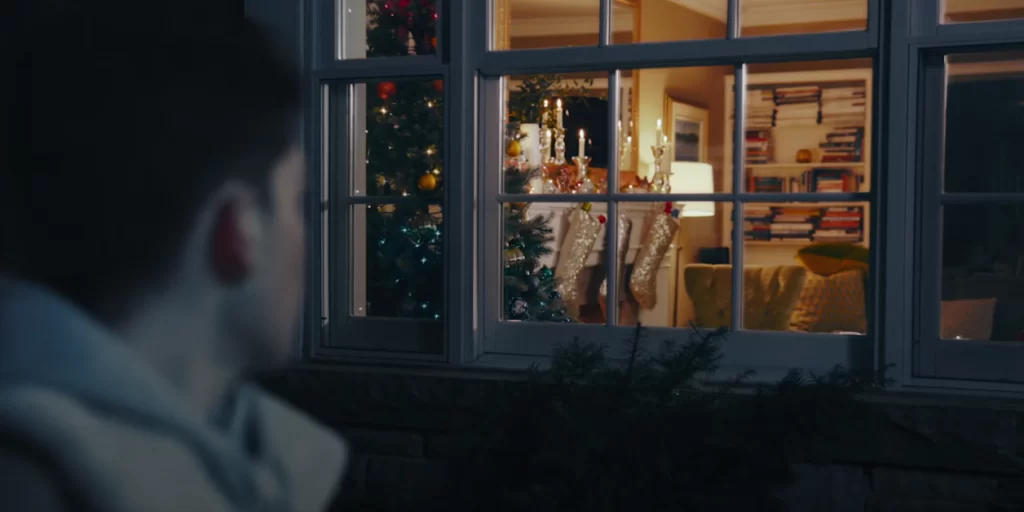 Youth looking into window with warm holiday decor from outside