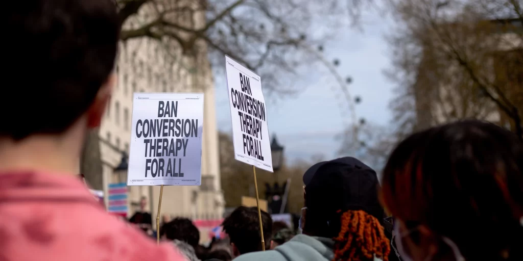 Rassemblement de protestation avec des pancartes indiquant "mettre fin à la thérapie de conversion pour tous"
